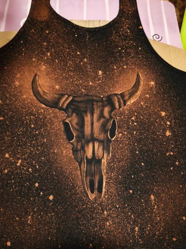 Tanktop im Country-Stil mit dem Bild eines Rinderschädels. 
Auf der Rückseite befindet sich im oberen Bereich eine Feder mit Perlen. 