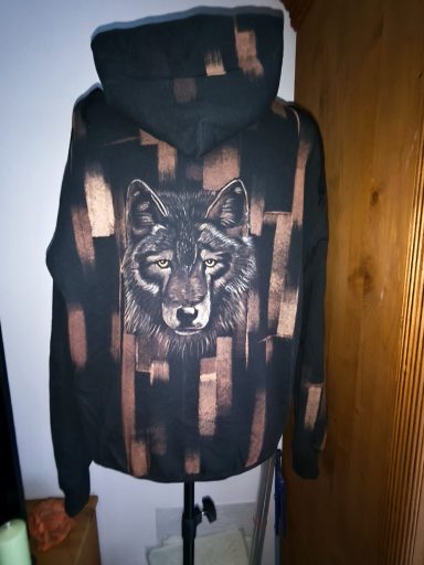 Hoodie mit Wolfskopf auf der Rückseite, vorne eine Wolfspfote. Graphischer Hintergrund, der sich auf dem Ärmel und der Kapuze wiederholt