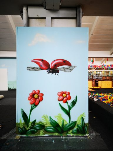 Bemalte Wand des Indoor Spielplatzes Wölpi. Marienkäfer fliegt über Blumen