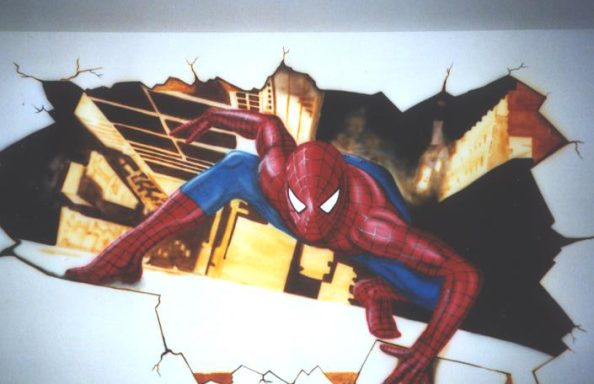 Man sieht einen gemalten Wanddurchbruch, wo Spiderman auf einem Fenstersims sitzt, mit Blick in die Stadt darunter.